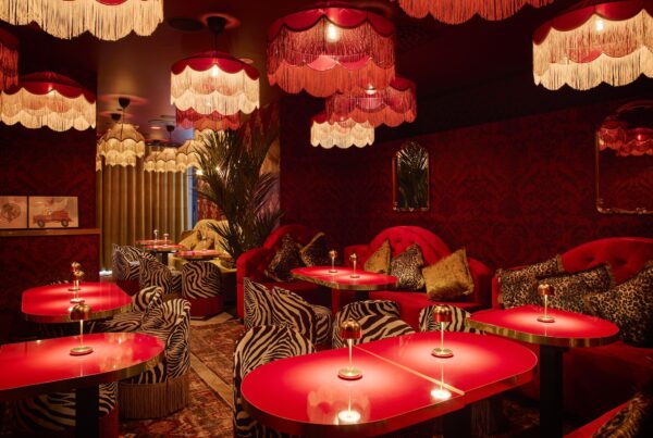 Glamorous restaurant interior with red lacquered tables, zebra and leopard print seating, and dramatic fringed pendant lights in warm red tones