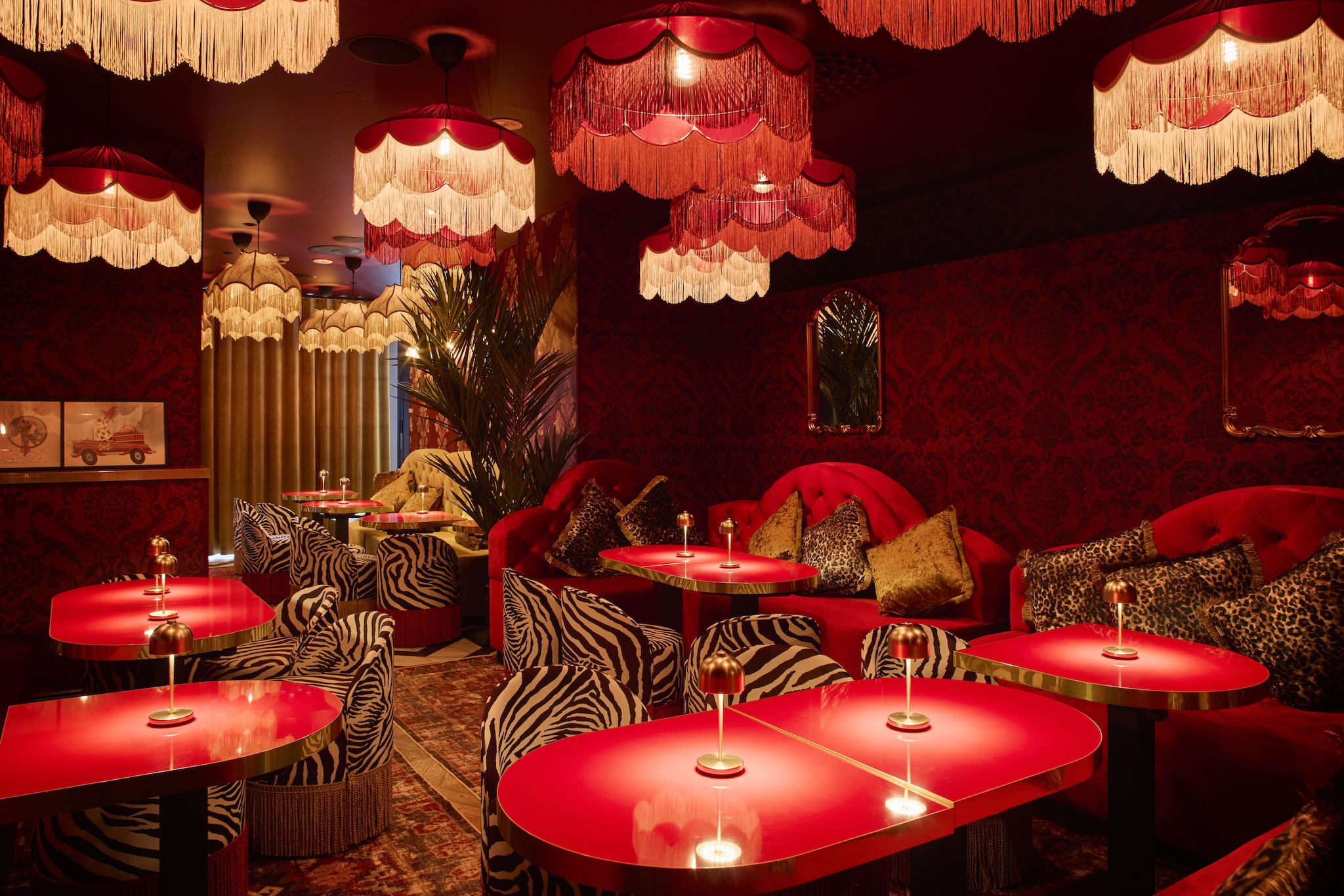 Glamorous restaurant interior with red lacquered tables, zebra and leopard print seating, and dramatic fringed pendant lights in warm red tones