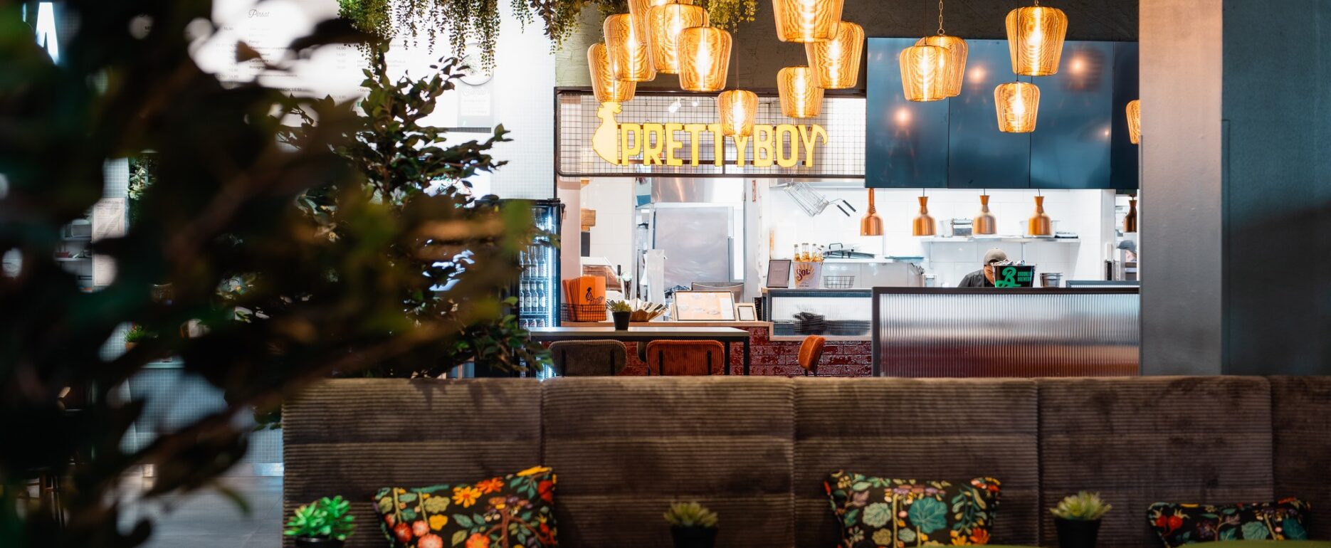 Pretty Boy restaurant neon sign above the open kitchen with pendant lights, booth seating and green tables