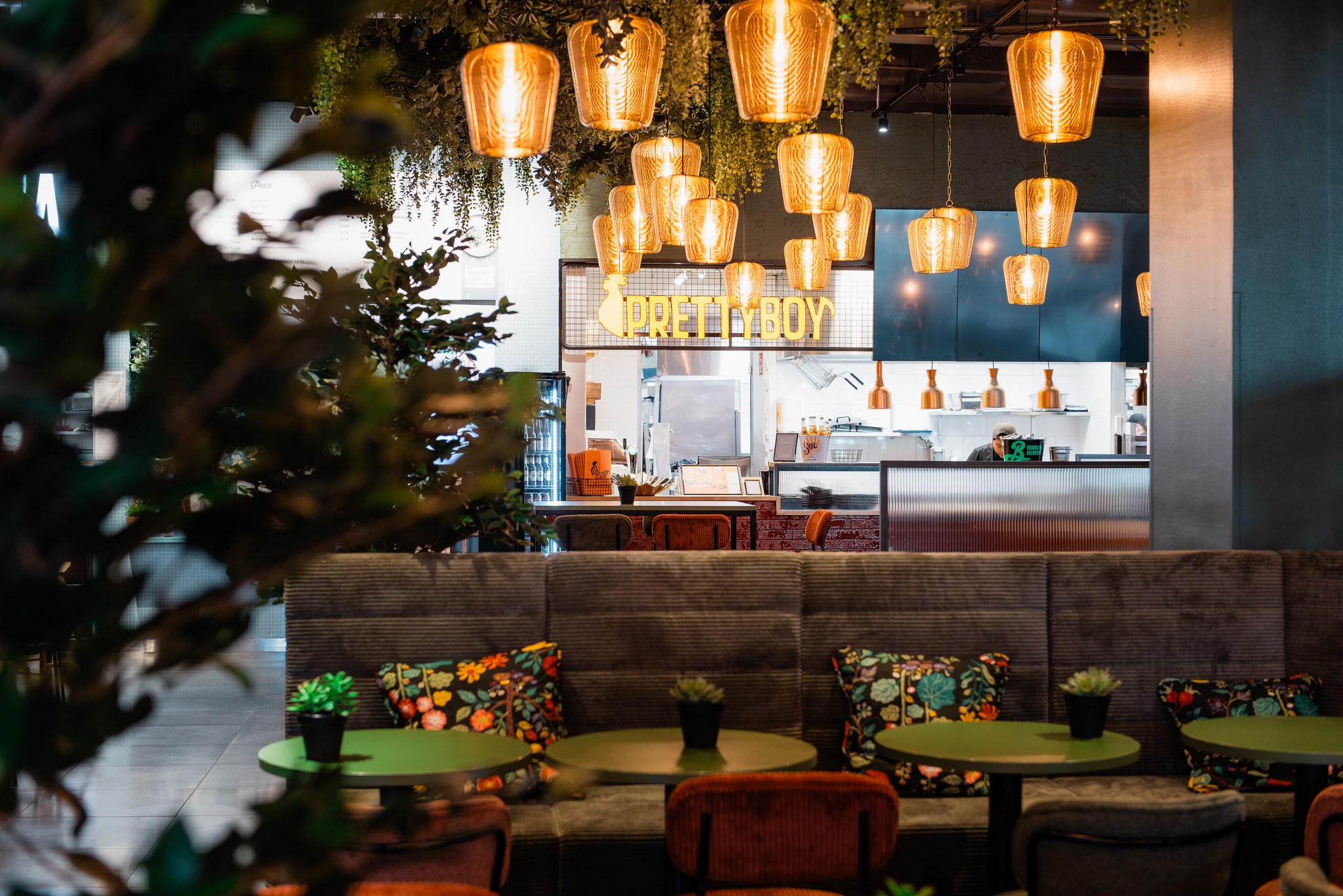 Pretty Boy restaurant neon sign above the open kitchen with pendant lights, booth seating and green tables