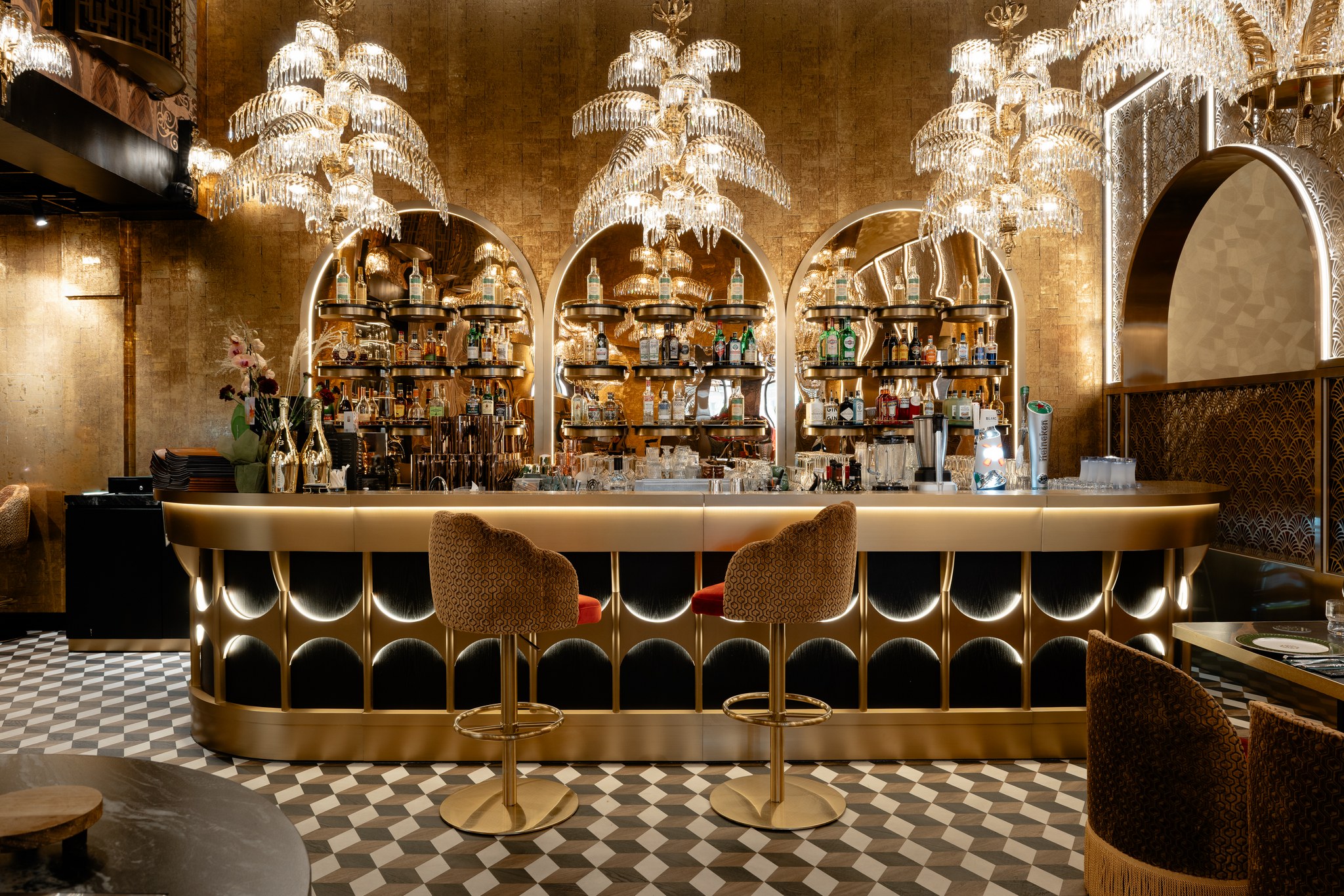 Gaucho Helsinki bar with gold-toned finishes, illuminated arched bottle displays, sculptural chandeliers and patterned flooring.